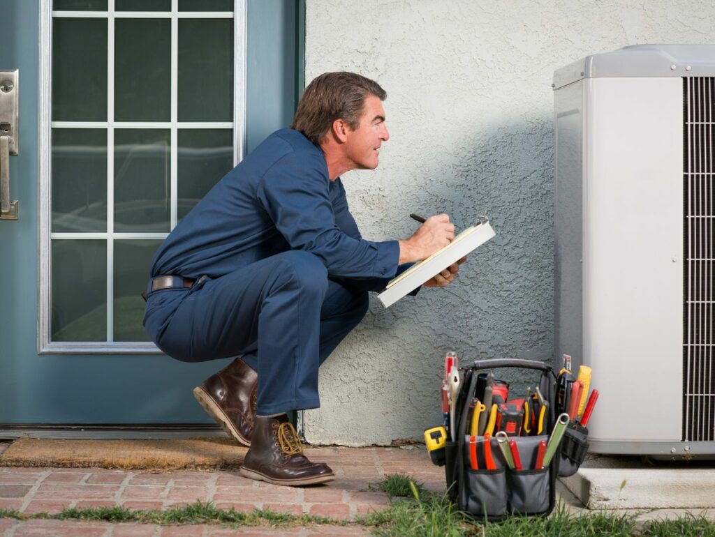 squatting man writing down air conditioner information